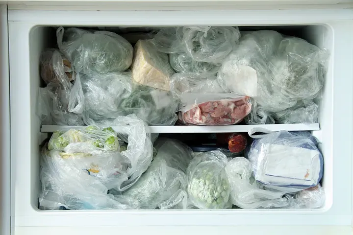 A freezer, very full with plastic-wrapped food.