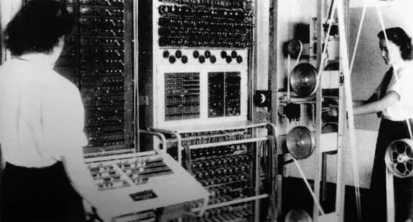 A black and white photo of two young women operating a large, complicated piece of equipment.