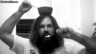 A man feeding himself from a bowl balanced on his head using a spoon in each hand.
