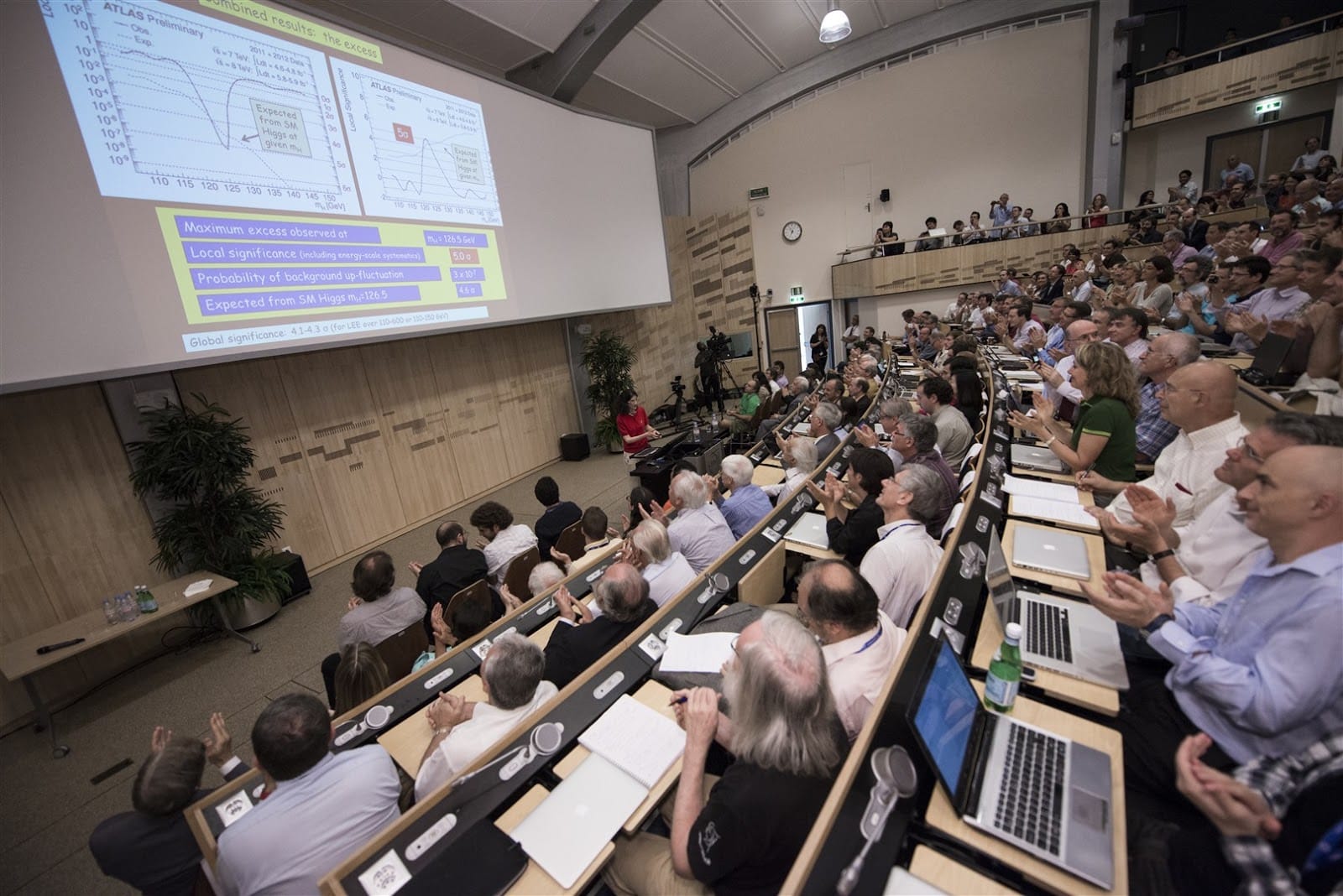 People sit in an auditorium looking at slides on a large screen.