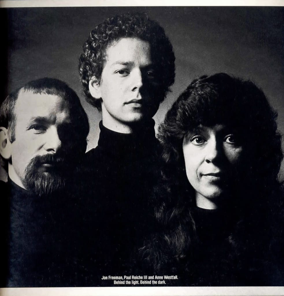 Two men and a woman in a group photo. They're all wearing black turtle-necked sweaters with neutral faces.
