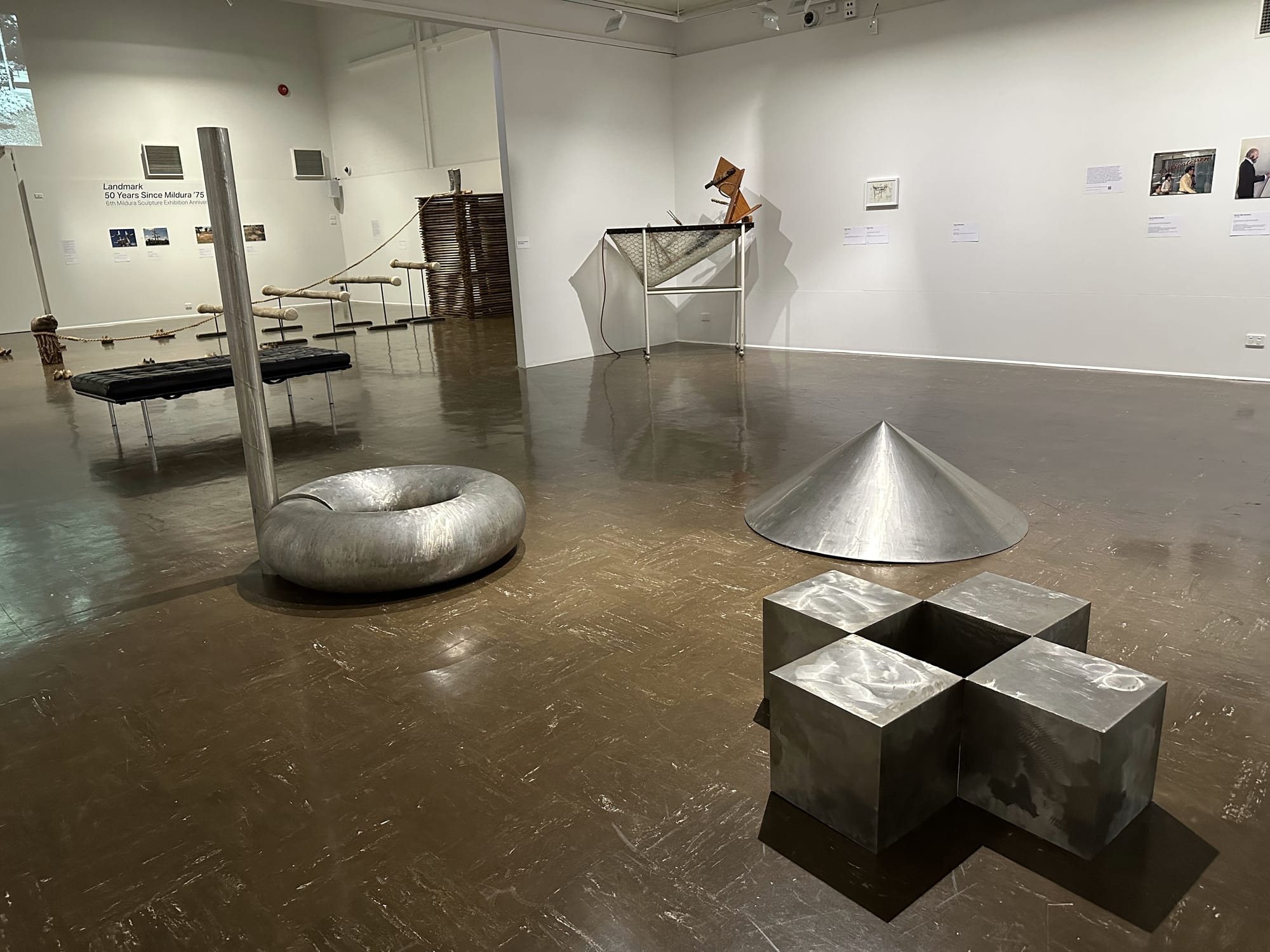 View from inside the Mildura Arts Centre 'Landmark' exhibition featuring stainless steel sculptures in silver cones, doughnuts and cubes.