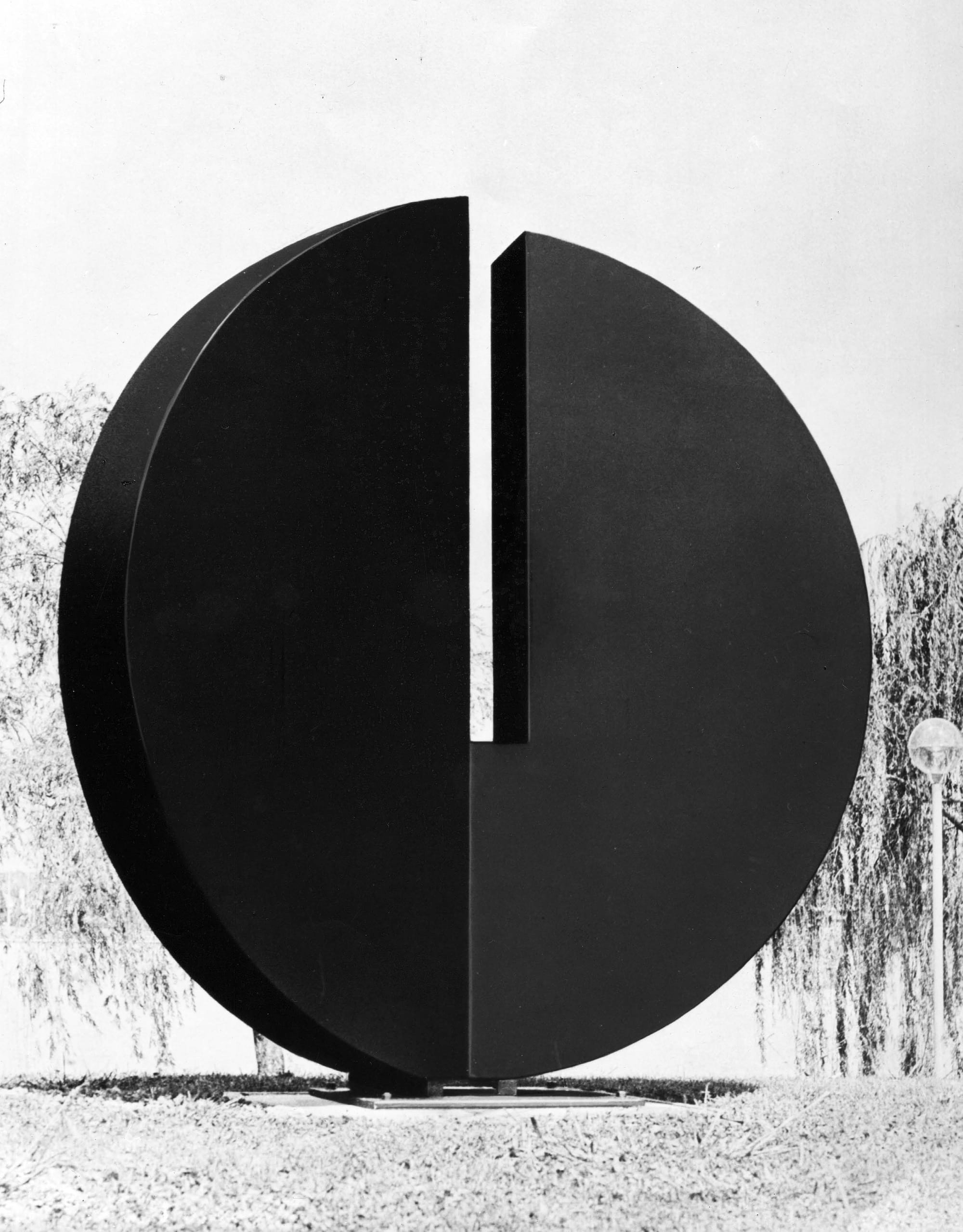 A black disk sculpture with a vertical slit from the top to the middle. 