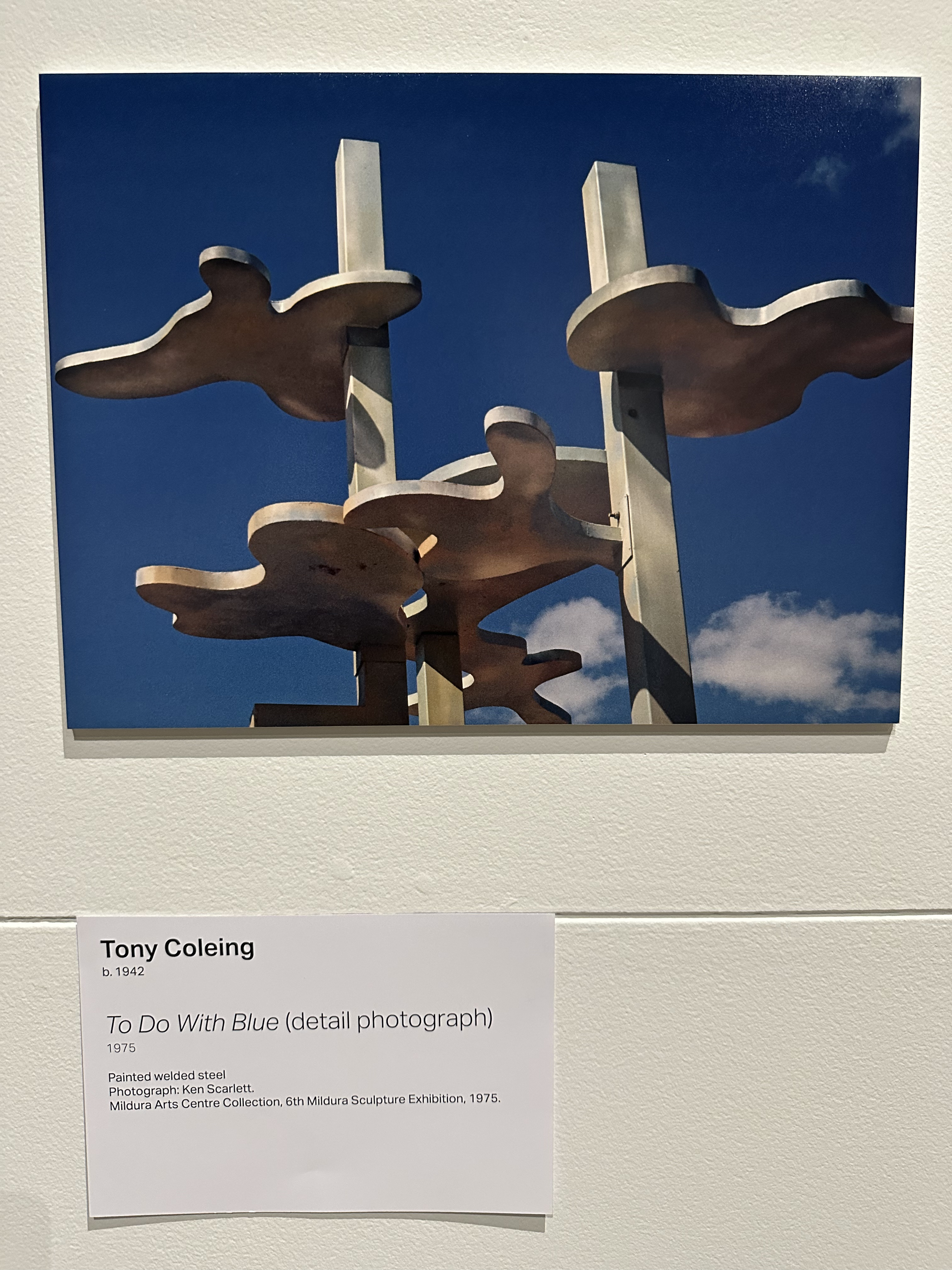 A photograph of a curvy metal sculpture with blue sky and soft white clouds in the background.