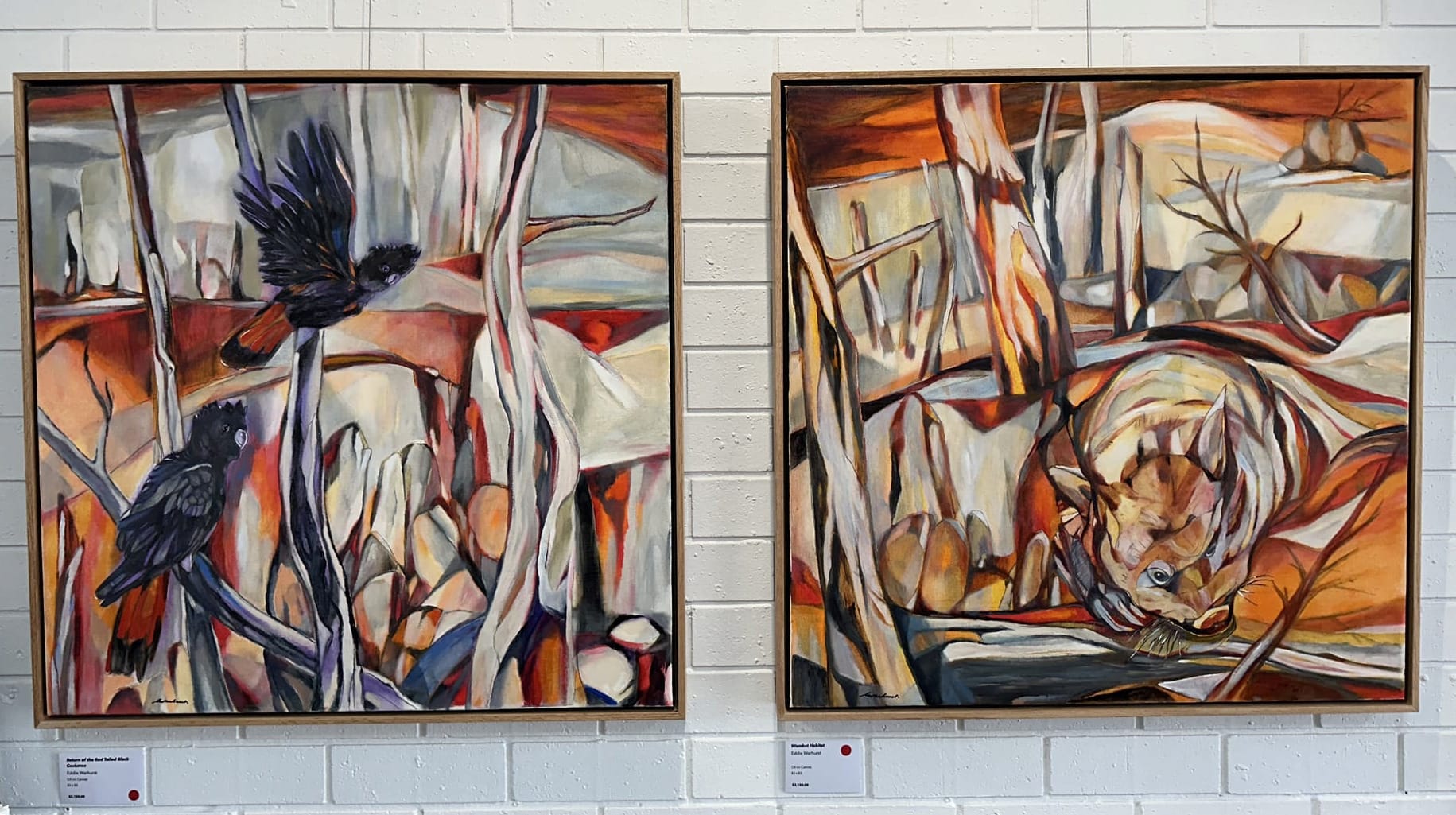 Two abstract colourful paintings with cockatoos and wombats on a white brick background.