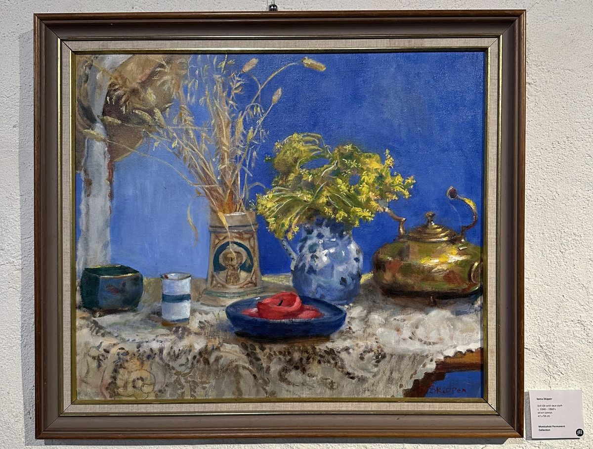 A table set with tea pot, red candle, vases with yellow flowers and grasses against a vibrant blue background