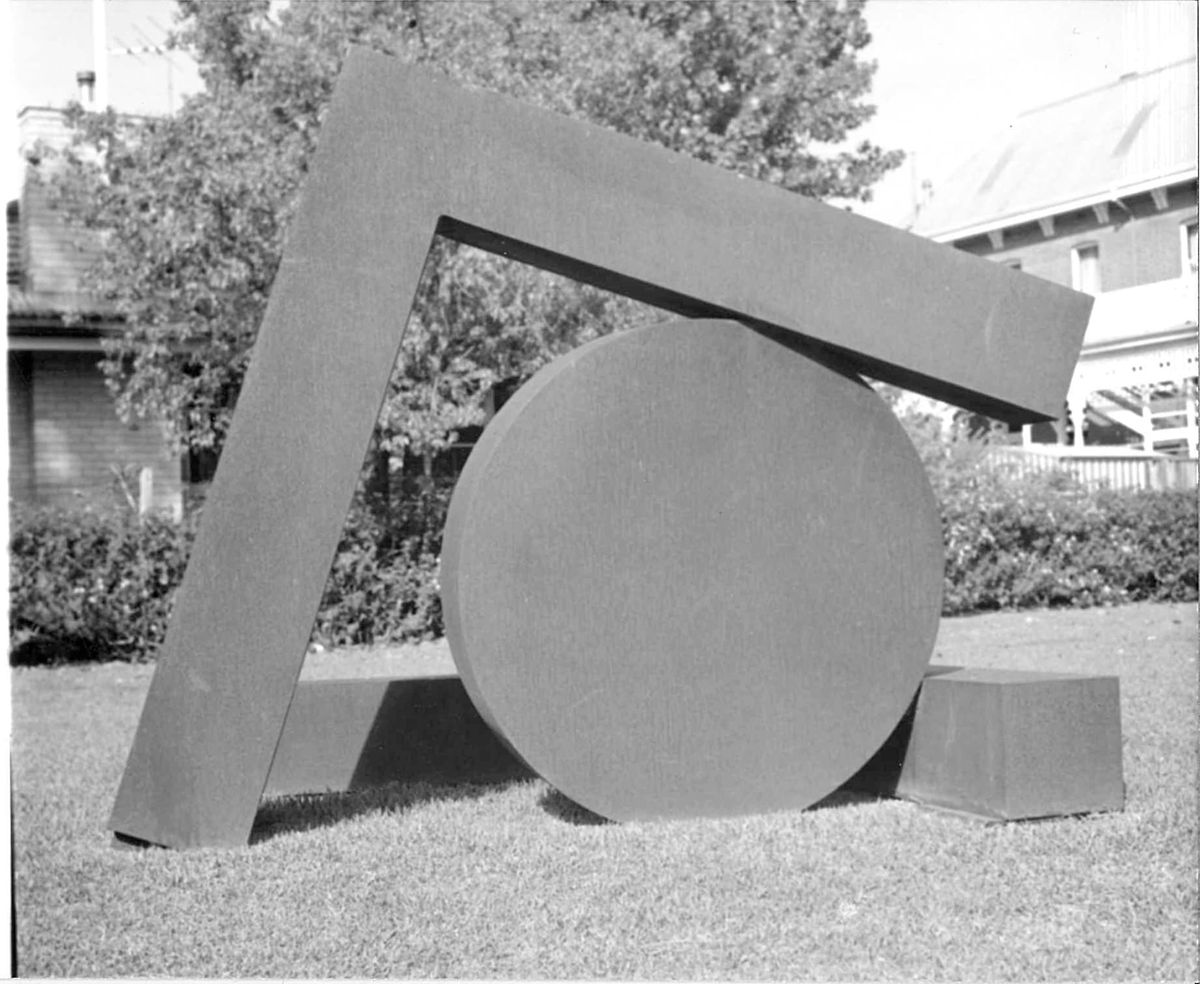A black and white photograph of a geometric sculpture, a round flat disk and a square armature encircling it.