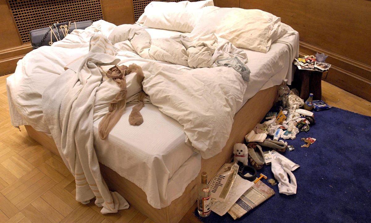The artist's unmade and messy bed displayed in a wooden walled gallery space.