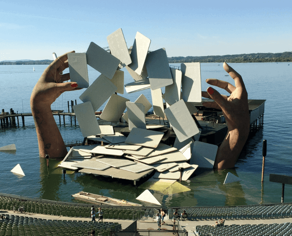 Stage on a lake show giant hands emerging from the water and a huge deck of cards