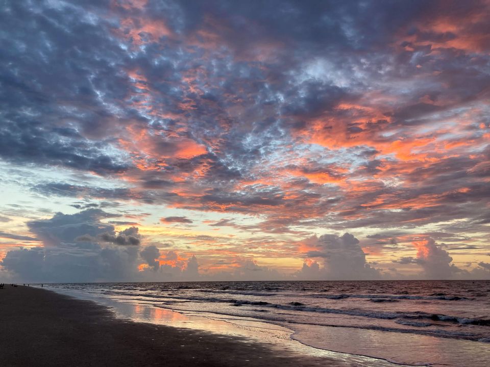 Orange and pink colored clouds in a big sky over an ocean seen from the beach
