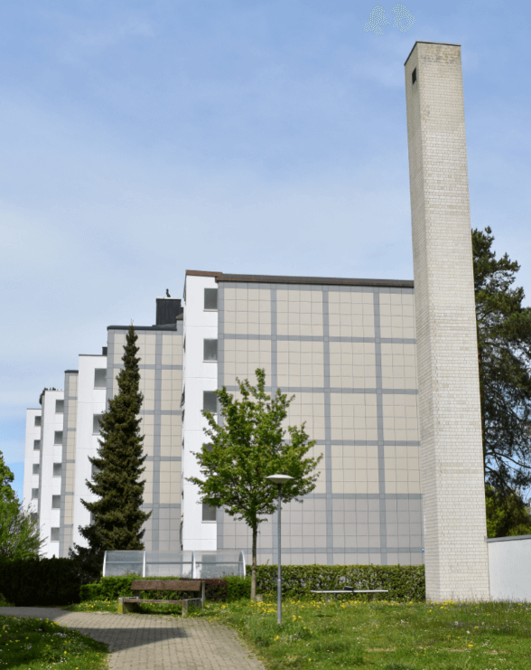 A geometric row of apartment buildings with a square smokestack in the foreground