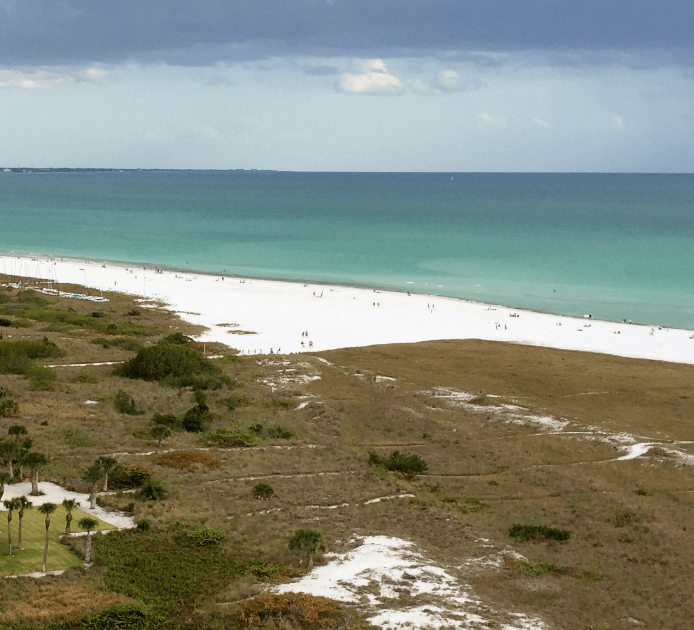 Long view of a white sand beach, with dunes in the foreground and the ocean in the background