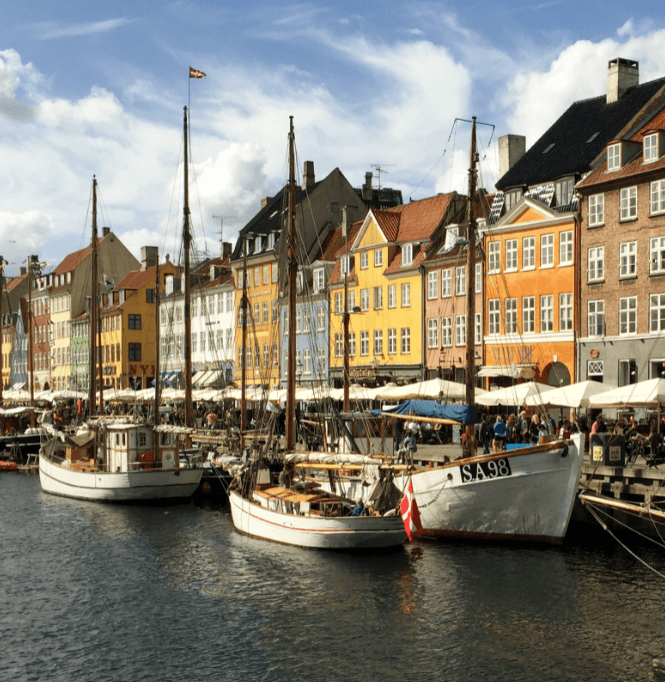 Sailing ships in a harbor alongside pastel-colored European houses
