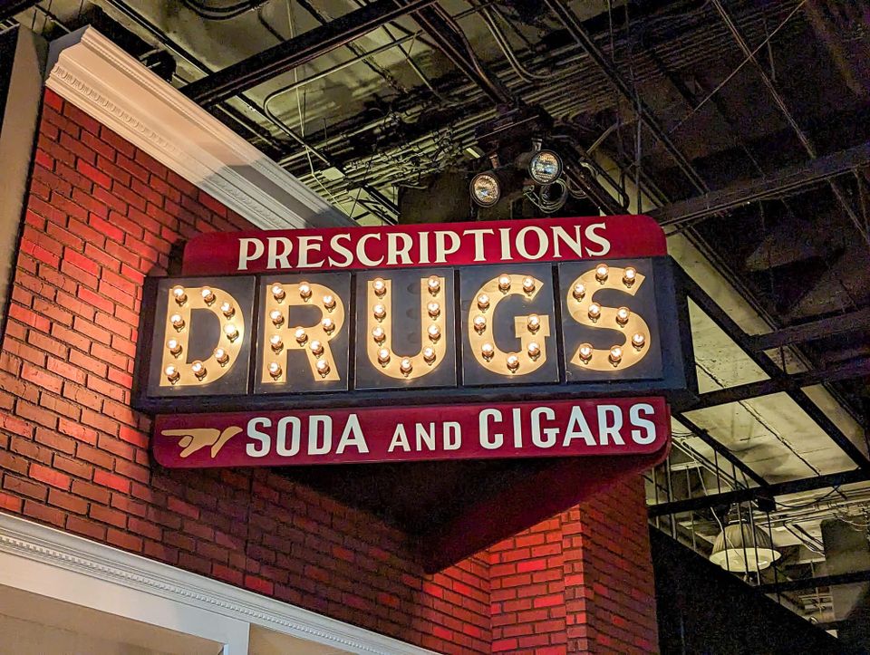 Store sign reading Prescriptions, DRUGS, Soda and Cigars.