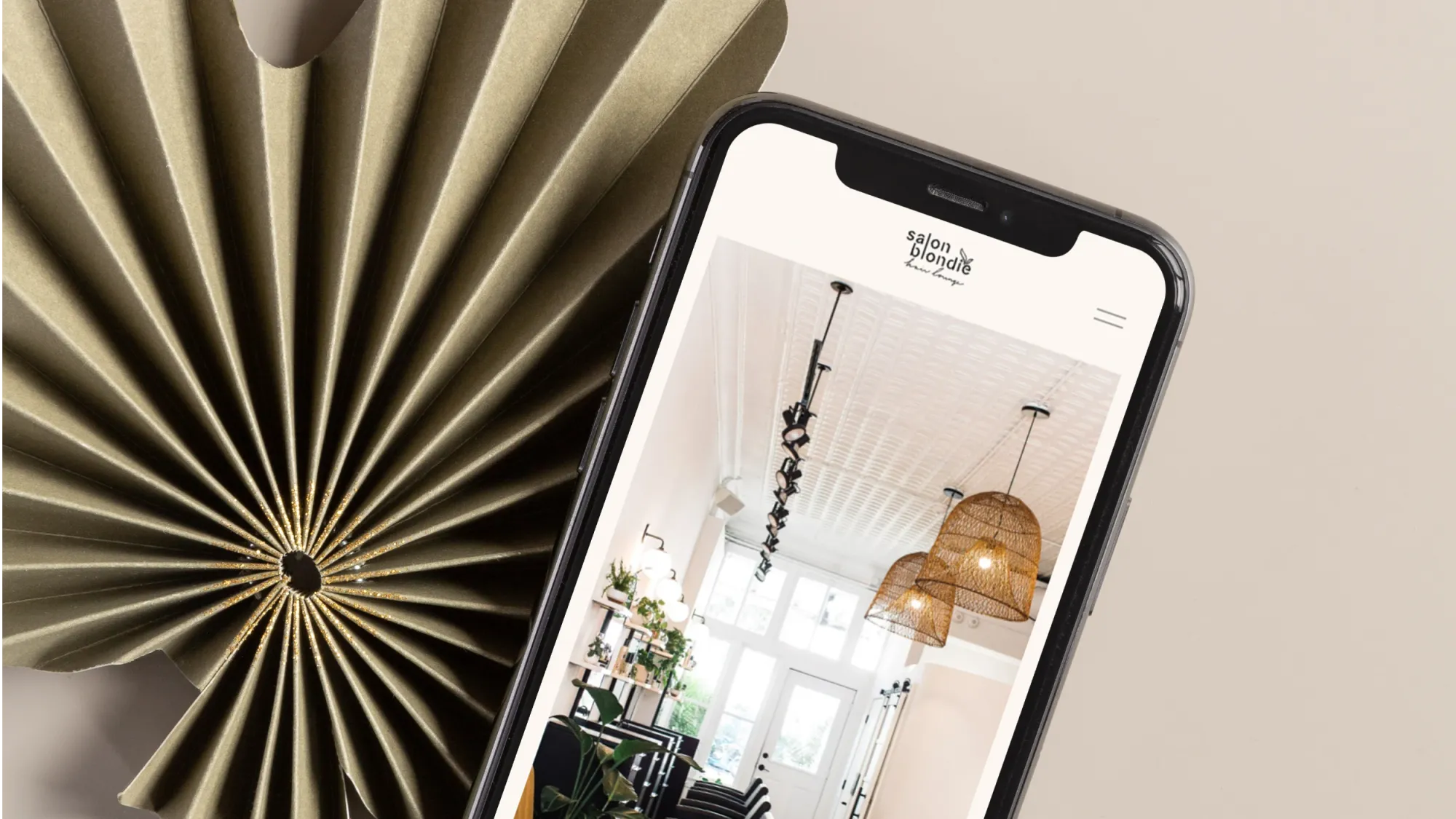 Salon Blondie's website displayed on an iPhone laying atop a paper palm leaf.