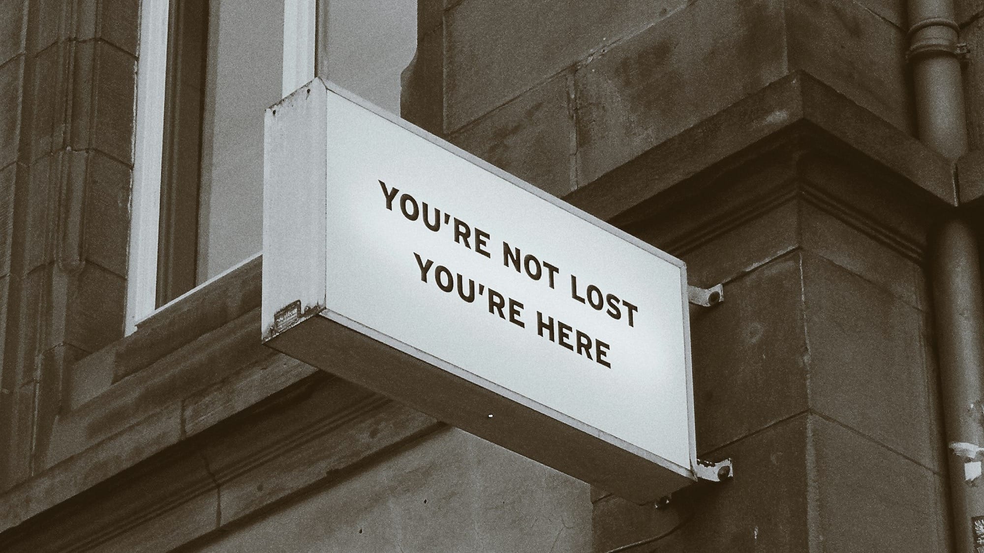 A building with a sign attached. The sign reads "You're not lost you're here."