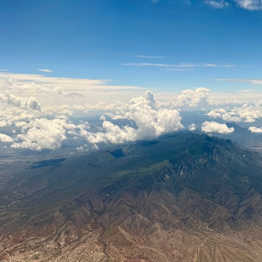 A rugged mountain flanked by a few clouds, with high clouds in the distance and blue skies overhead.