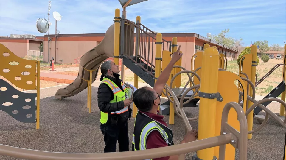 Two people wearing safety vests are looking at a school playground