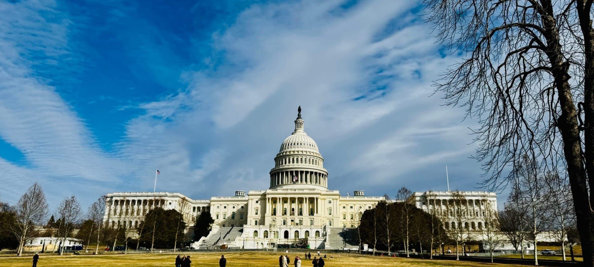 The U.S. Capitol building, lit by sunlight, with partly cloudy skies overhead.