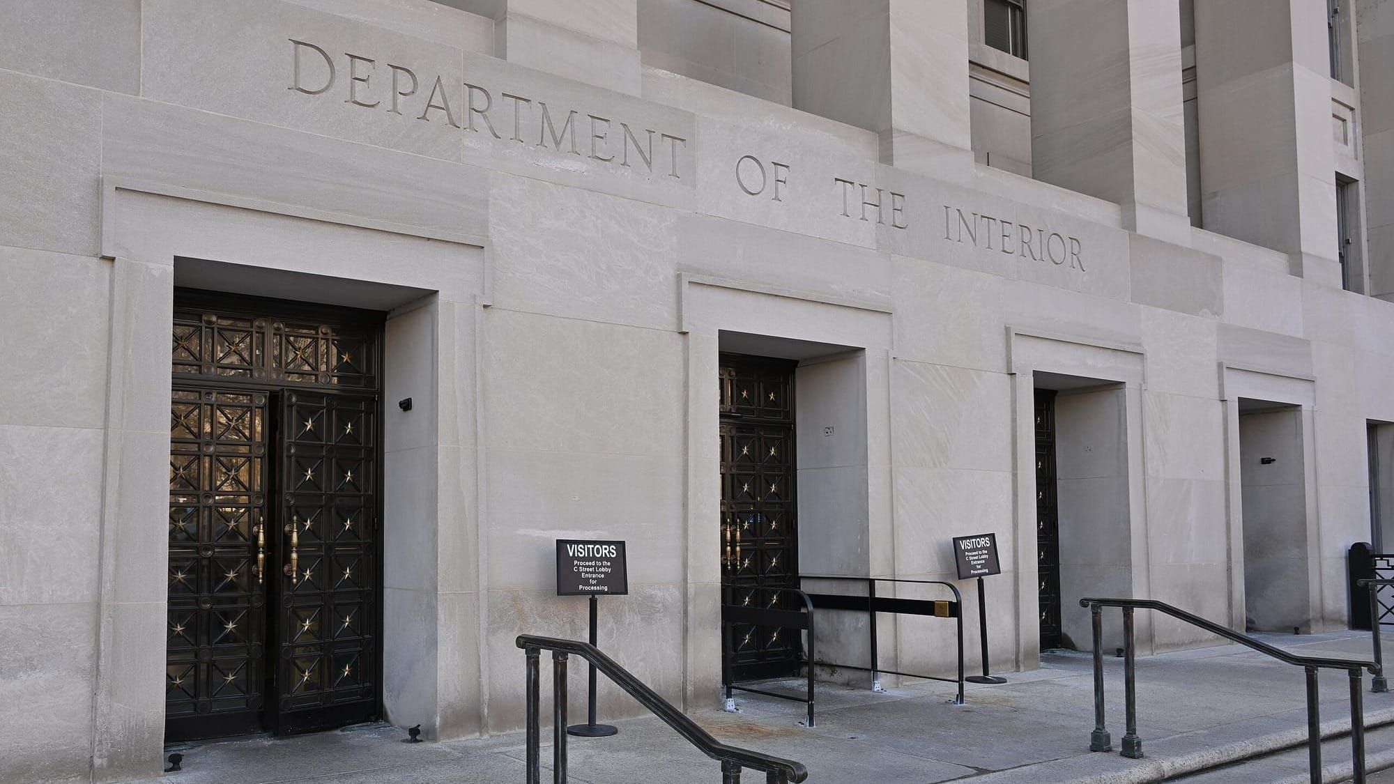 Front of a stone building with four doors visible, and the words "Department of the Interior" inscribed above the doors.