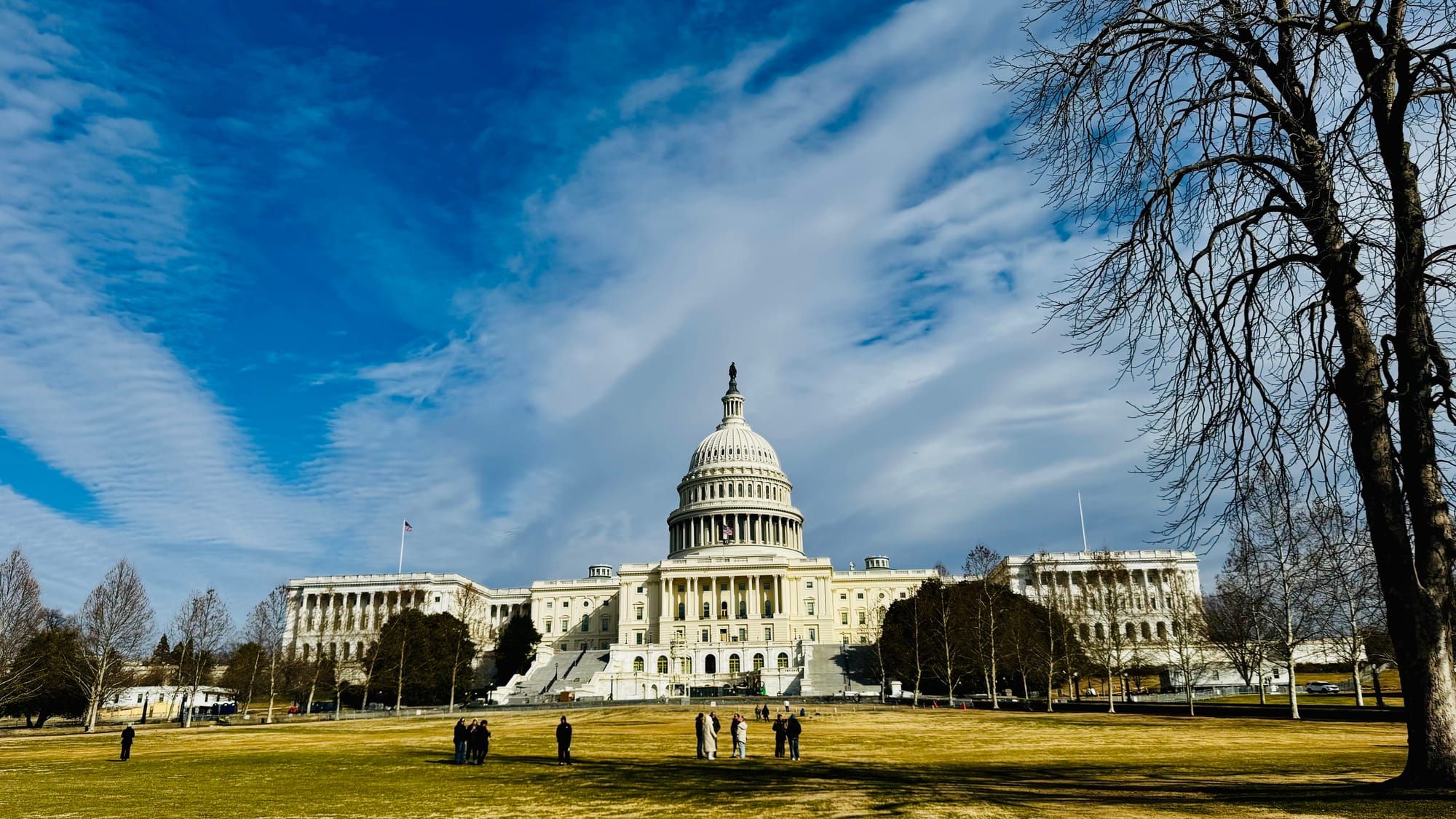 The US Capitol Building in winter under partly cloudy skies, with people standing out front.