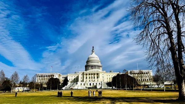 The U.S. Capitol Building under partly cloudy skies, and with a few people standing in the foreground.