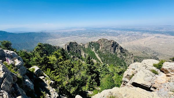 View intod a desert valley from a rocky outcrop under clear skies, with smoke in the distance.