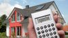 A person's hand holding a calculator in front of a house 