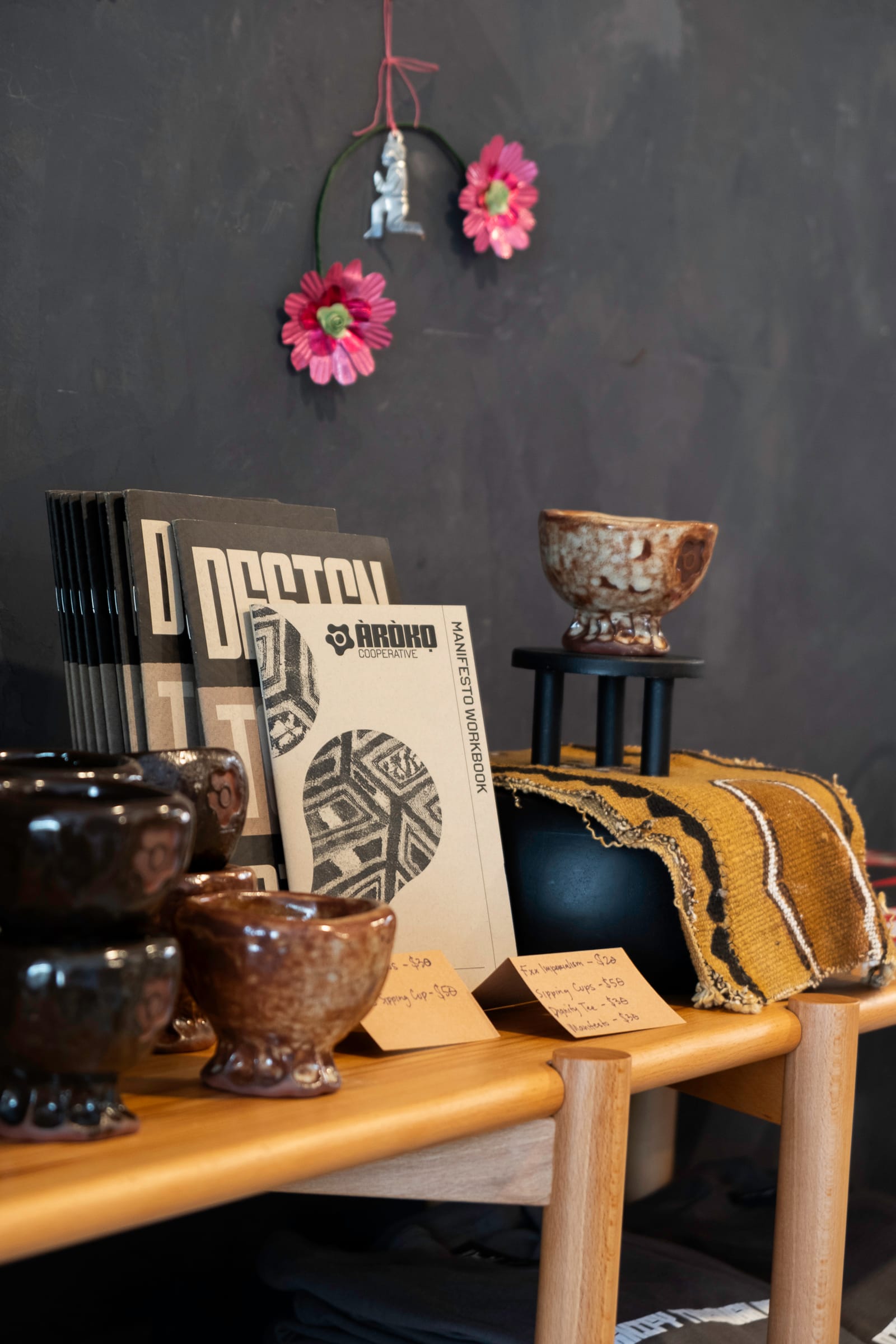 Display of products including handmade ceramic cups with the Àròko logo, as well as the physical version of the Design to Divest Manifesto.