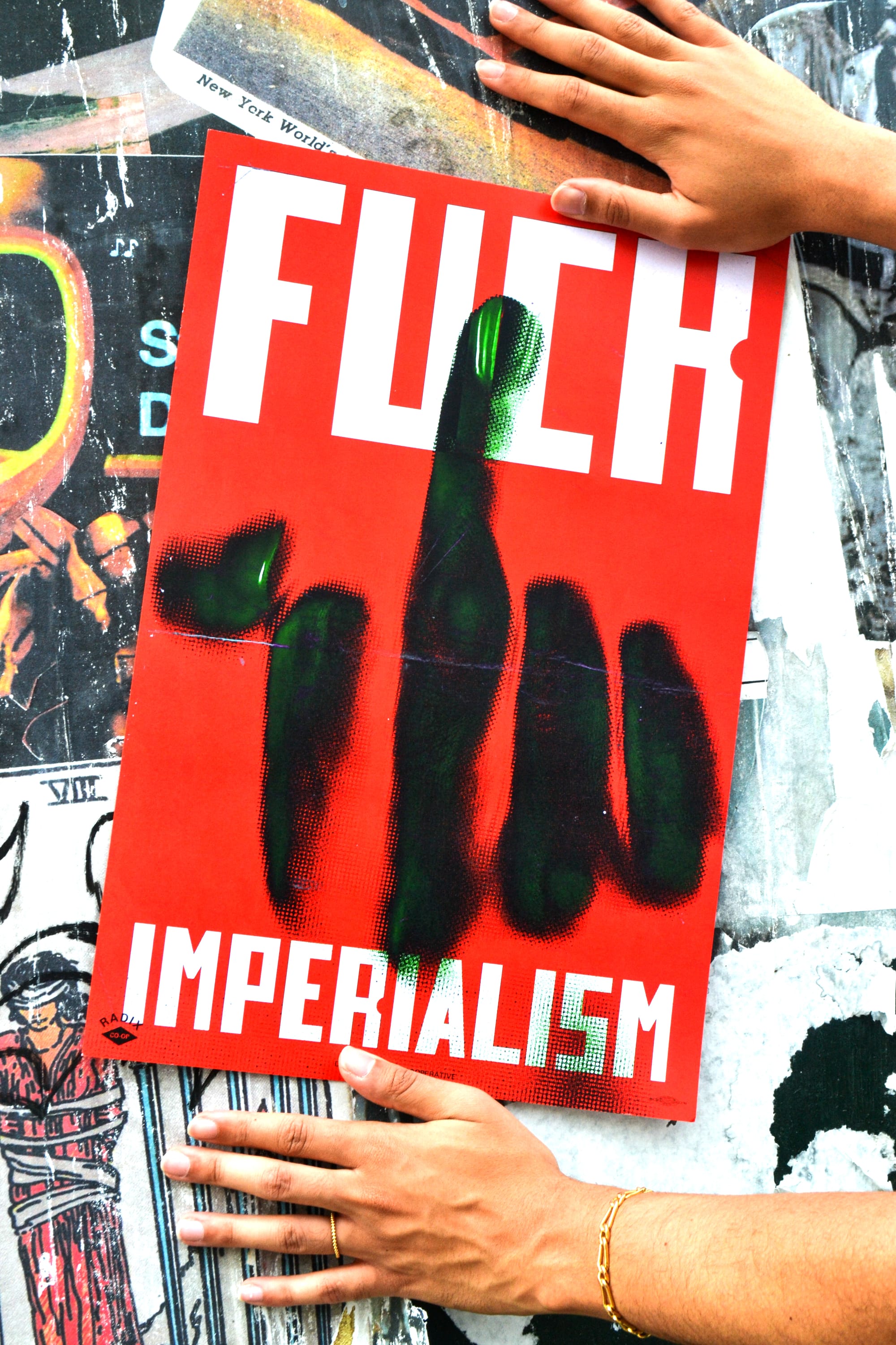 A poster with the words 'FUCK IMPERIALISM' and a large middle finger is being put up on a construction barrier.