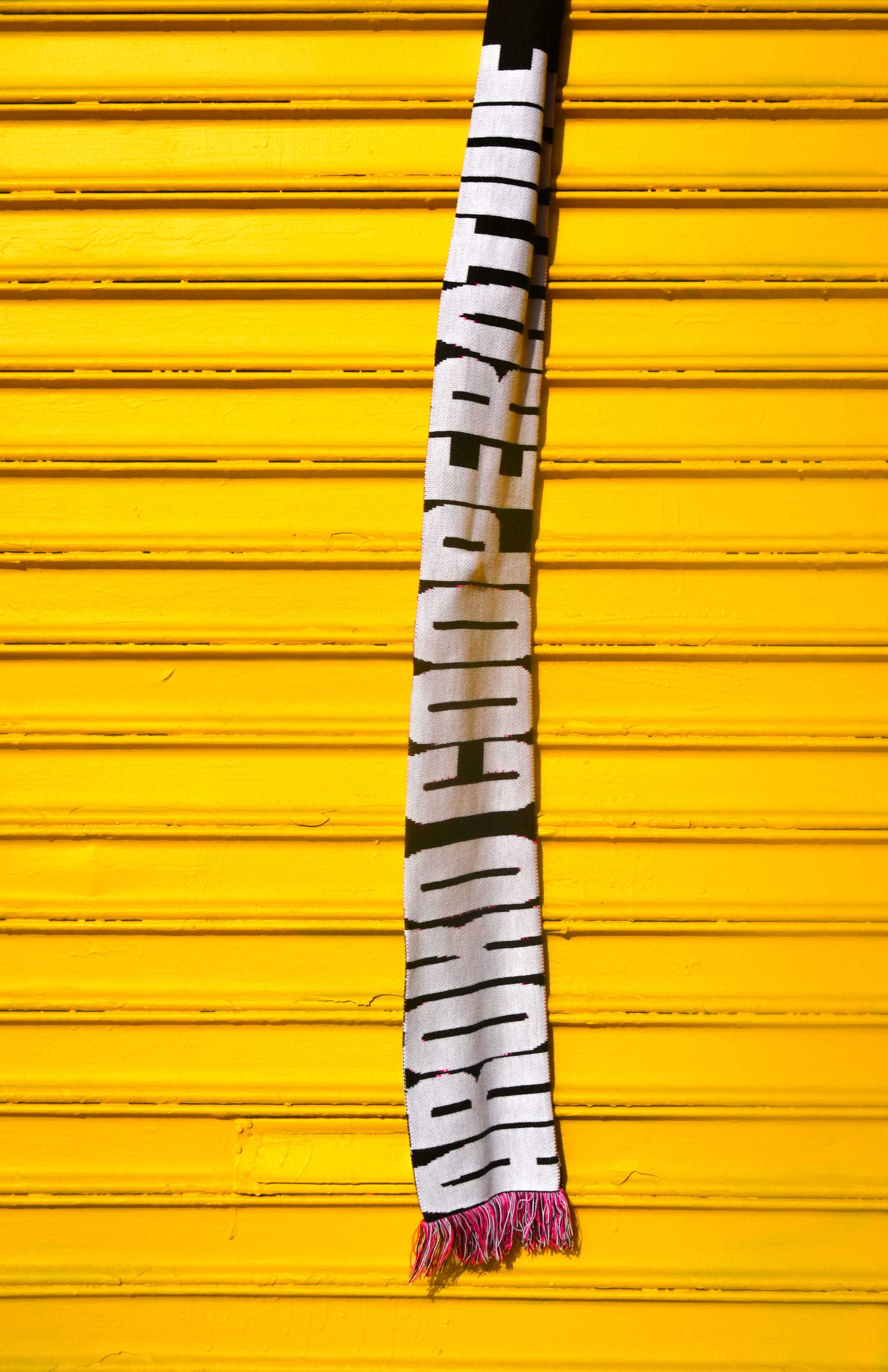 A scarf with the words 'AROKO COOPERATIVE' hangs vertically in front of a yellow garage door.