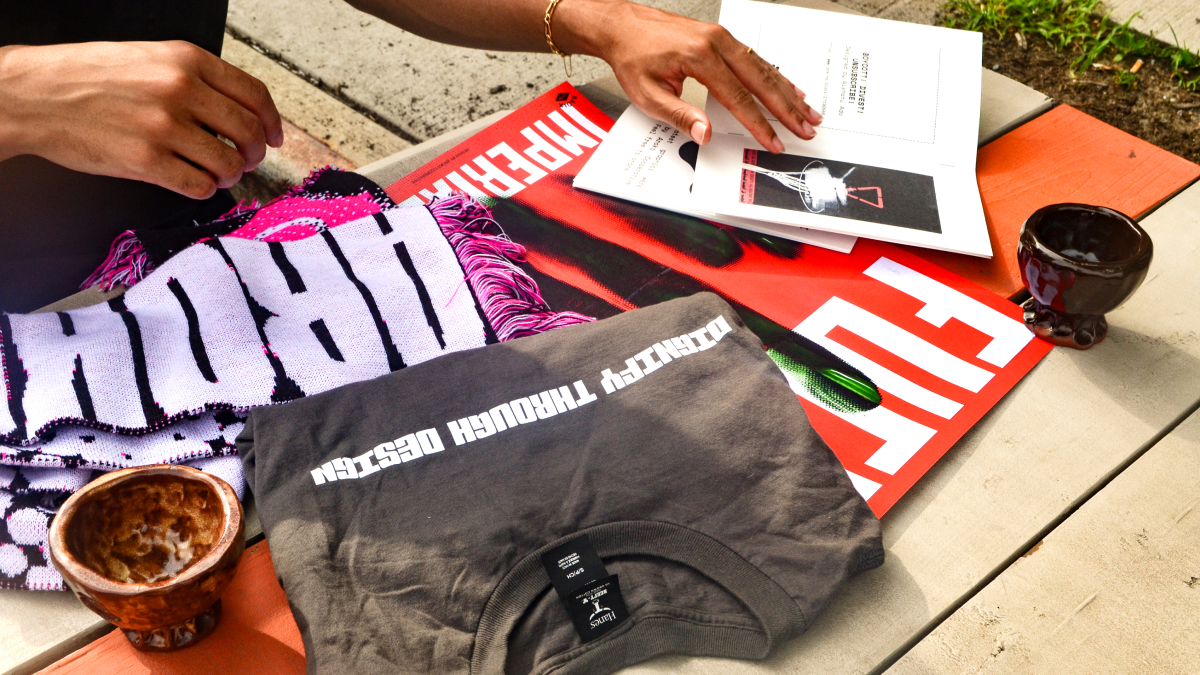 Photograph featuring the full range of products from Àrokò's first capsule collection, including a scarf, a t-shirt, 2 cermaic cups, a poster, and a zine.