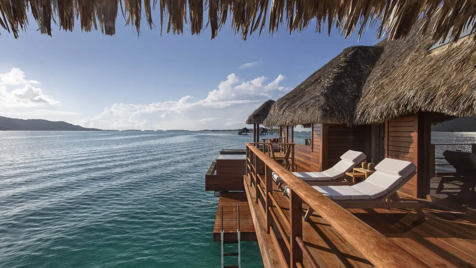 An overwater bungalow's private lanai with sun loungers above the turquoise lagoon at Four Seasons Bora Bora