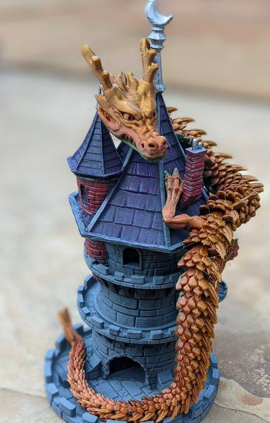 A close-up of a multi-colored 3D printed dragon coiled around a castle tower, highlighting the intricate details and articulation of the dragon's scales and the architectural features.