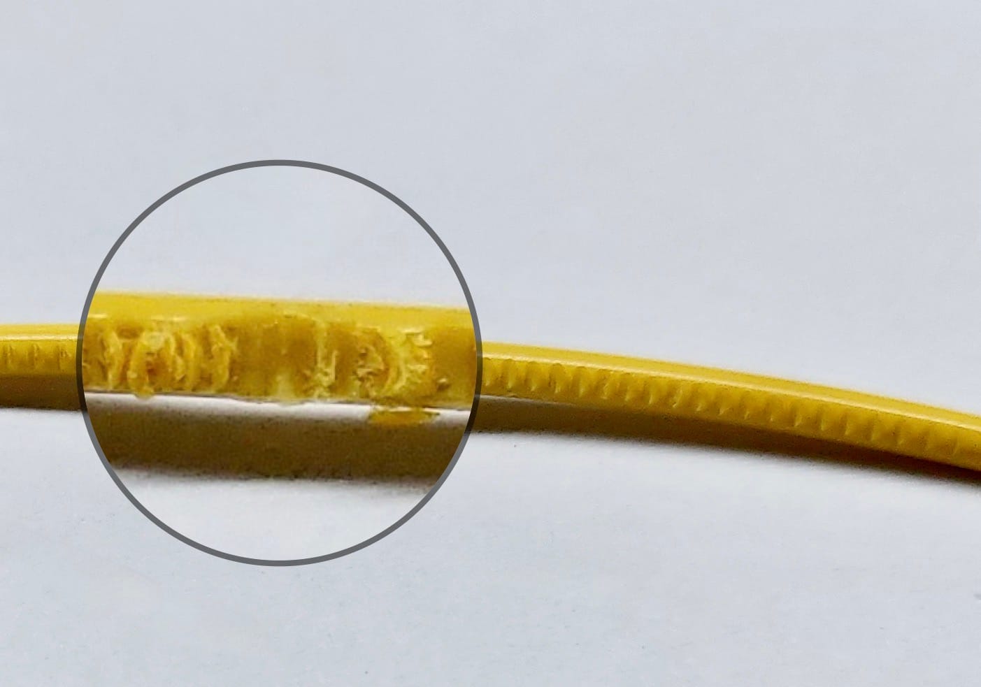A close-up photo of a yellow 3D printing filament with a circled section showing visible damage and deformation, indicating issues that can contribute to a nozzle jam during printing.