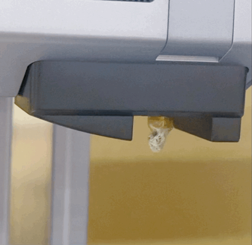 A heated 3D printer nozzle being cleaned with tweezers, removing melted filament residue from the nozzle's exterior. This demonstrates proper maintenance to prevent nozzle clogs.
