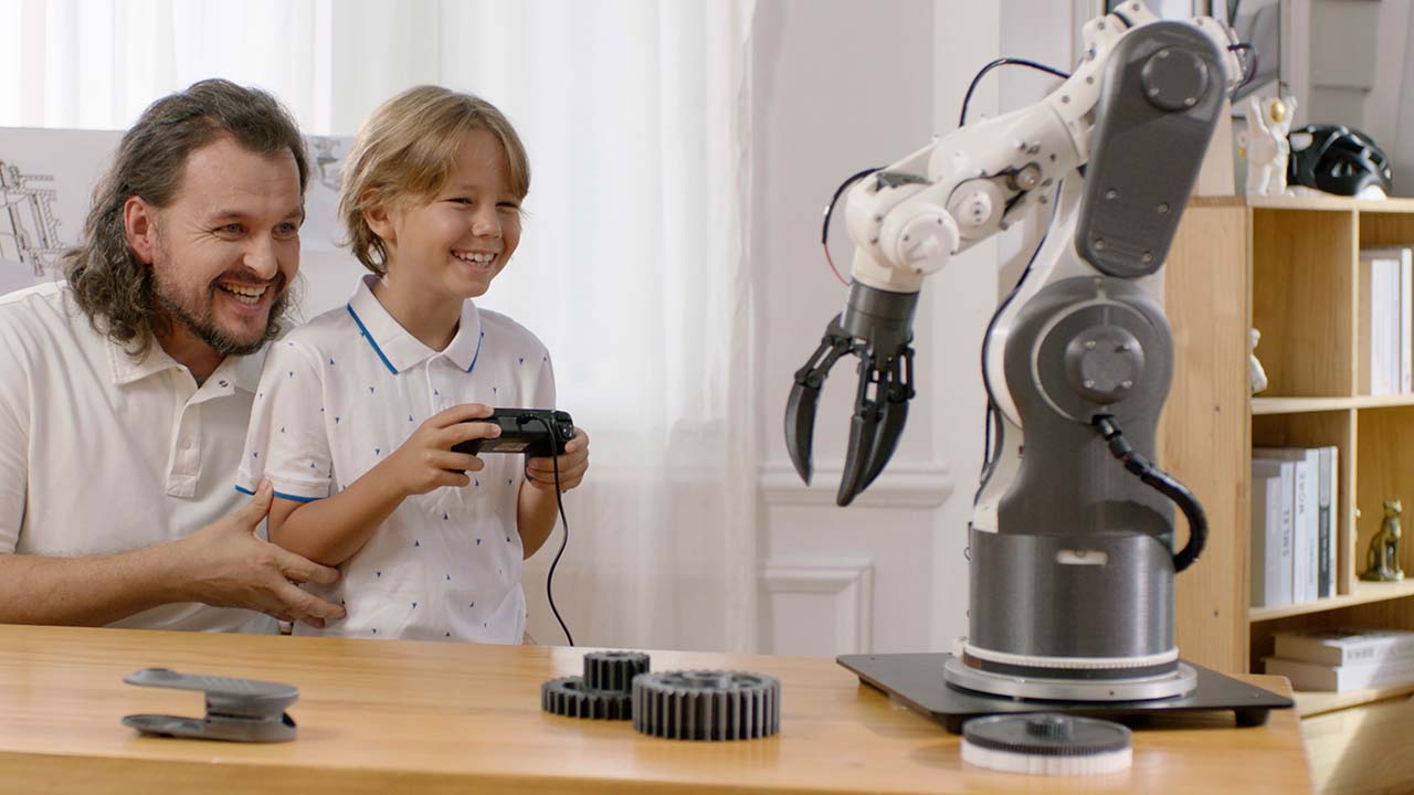 A man and a boy enjoying a robotic arm, illustrating the advanced manufacturing possibilities that modern multi-material 3D printers enable.