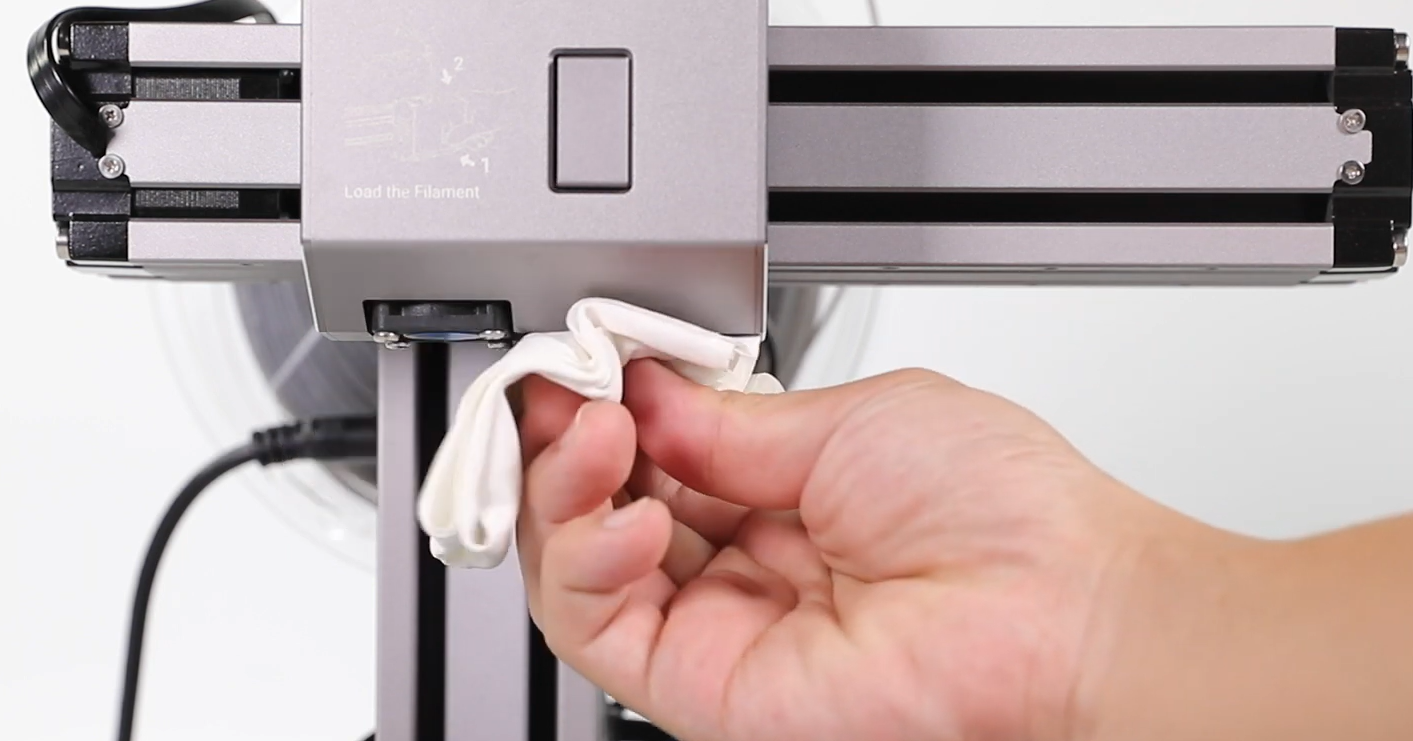 Close-up of a hand wiping a 3D printer nozzle with a cloth to improve first layer adhesion.