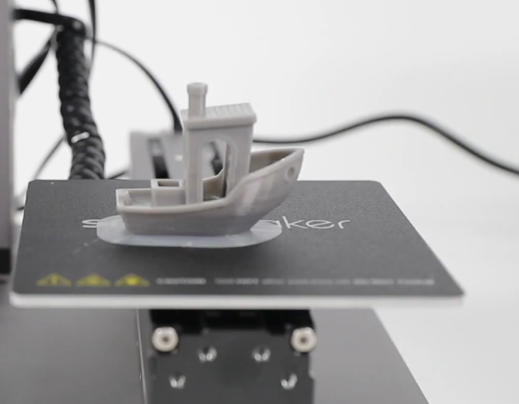 A 3D printed Benchy boat model on a Snapmaker printer with a clearly visible brim, indicating a successful first layer adhesion.