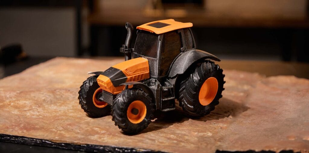 3D-printed toy tractor using dual-color filament in black and orange.