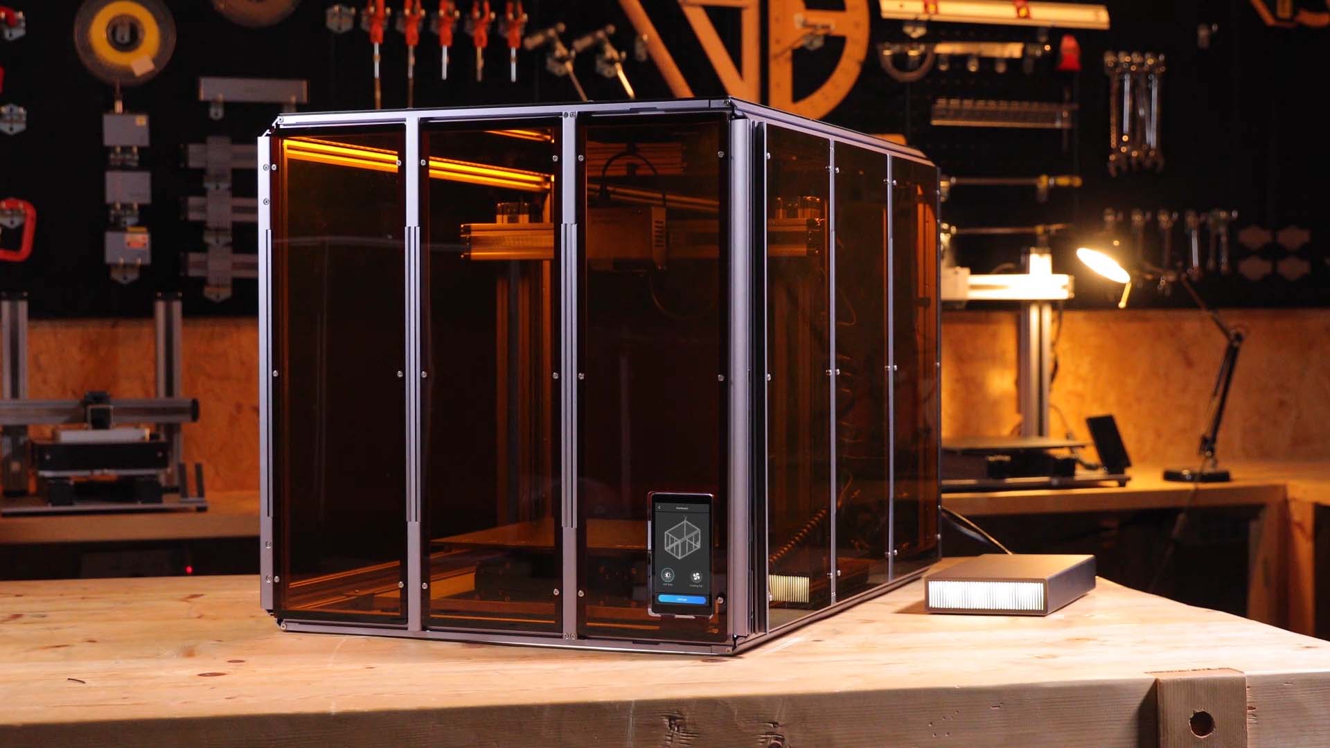 A complete 3D printer safety setup in a workshop, showing the printer inside a large enclosure with an air purifier system placed next to it for fume extraction.