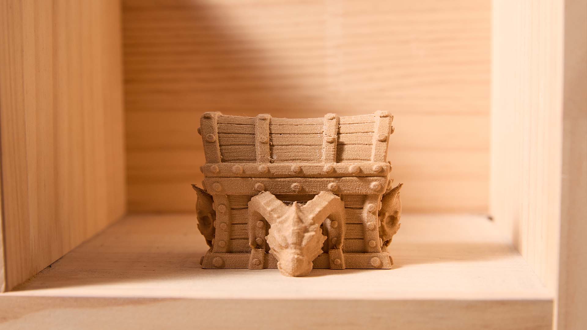 A detailed, 3D printed treasure chest with a dragon skull on the front, showcasing the realistic texture achievable with wood PLA filament.
