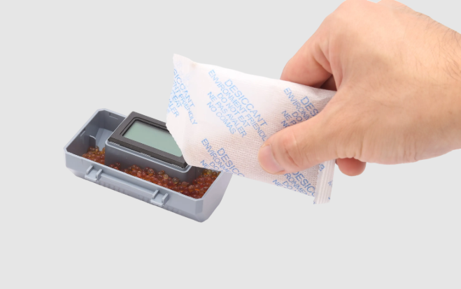 A hand placing a desiccant packet into a container of silica gel beads to absorb moisture and protect 3D printer filament.
