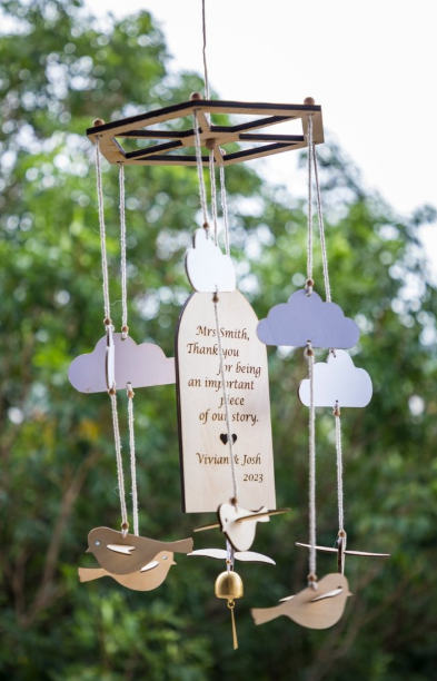 Hanging outdoors is a personalized laser-engraved wind chime with a message of gratitude, decorated with bird and cloud motifs and a small brass bell.