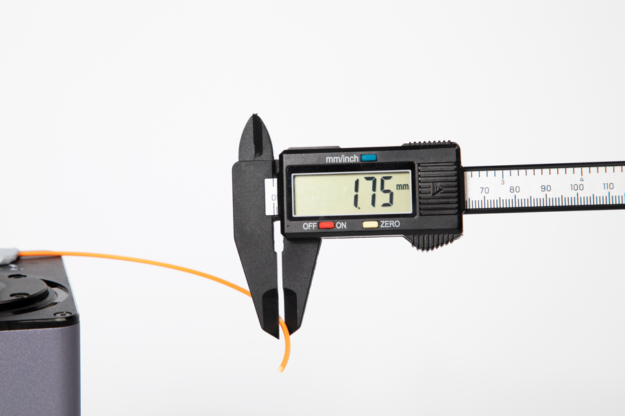  A digital caliper measuring the diameter of a piece of orange 3D printer filament, with the screen displaying a reading of 1.75 mm.