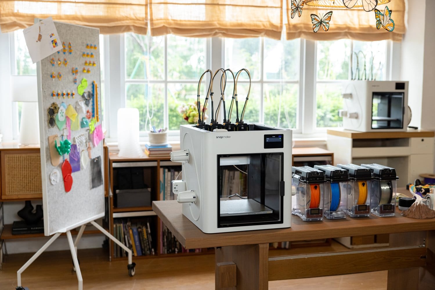 A professional multi-color 3D printer (Snapmaker U1) on a workbench next to several enclosed filament cartridges, showcasing an organized printing and storage workflow.