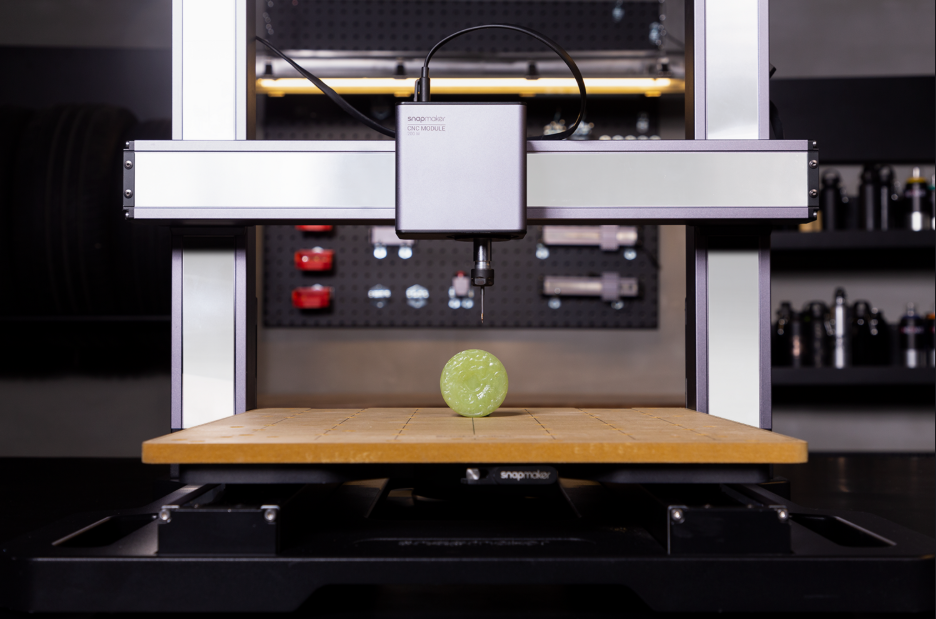 The Snapmaker CNC module poised to carve an intricate design into a small, spherical piece of green jade stone.