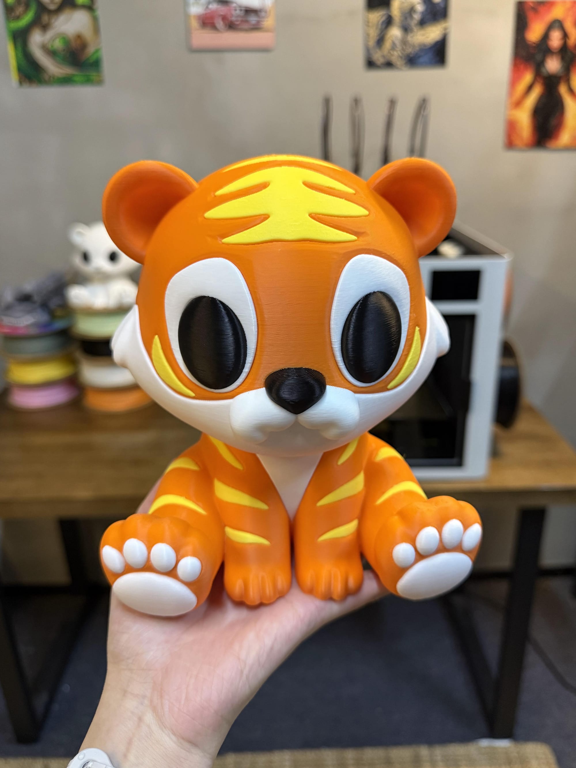 A person holds up a finished multicolor 3D print of a cute tiger cub, showing the sharp, clean lines between the orange, yellow, white, and black filament.