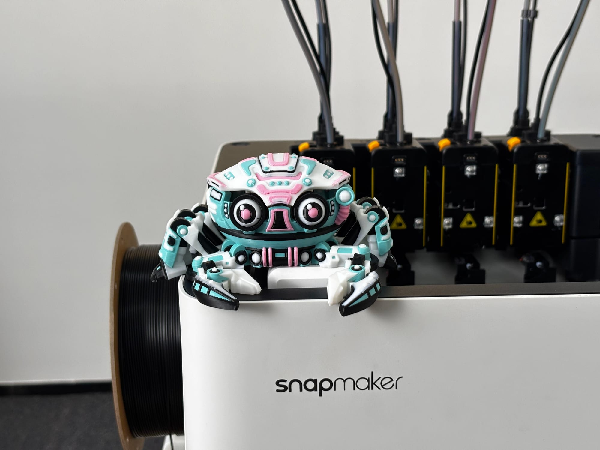 A multicolor articulated 3D printed Cyber Crab toy with pink, blue, and white details sits on the edge of a Snapmaker printer, showcasing a functional print-in-place model.