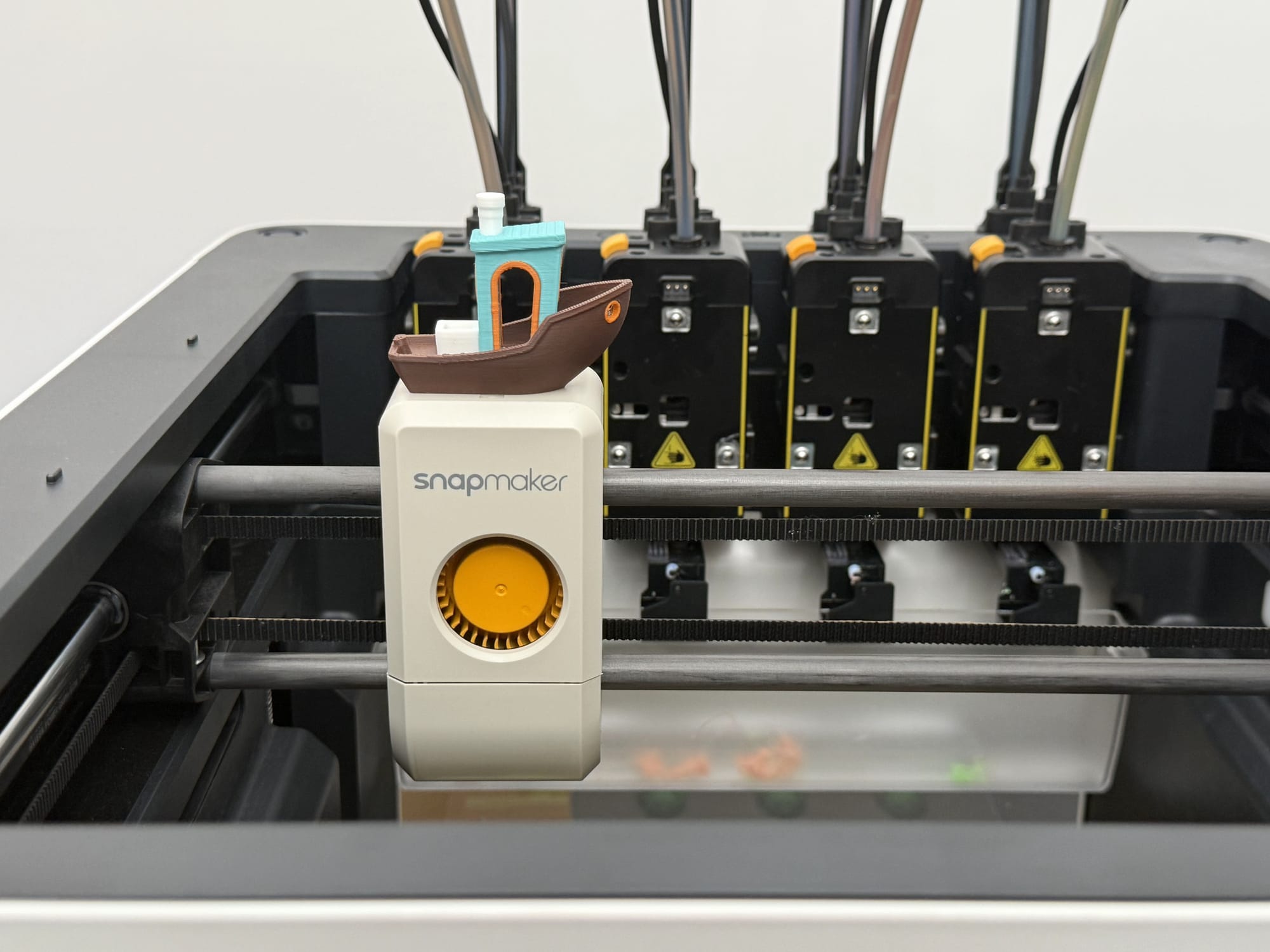 A four-color 3D printed Benchy model sits on the print head of a Snapmaker 3D printer, showcasing a clean and precise multicolor print.